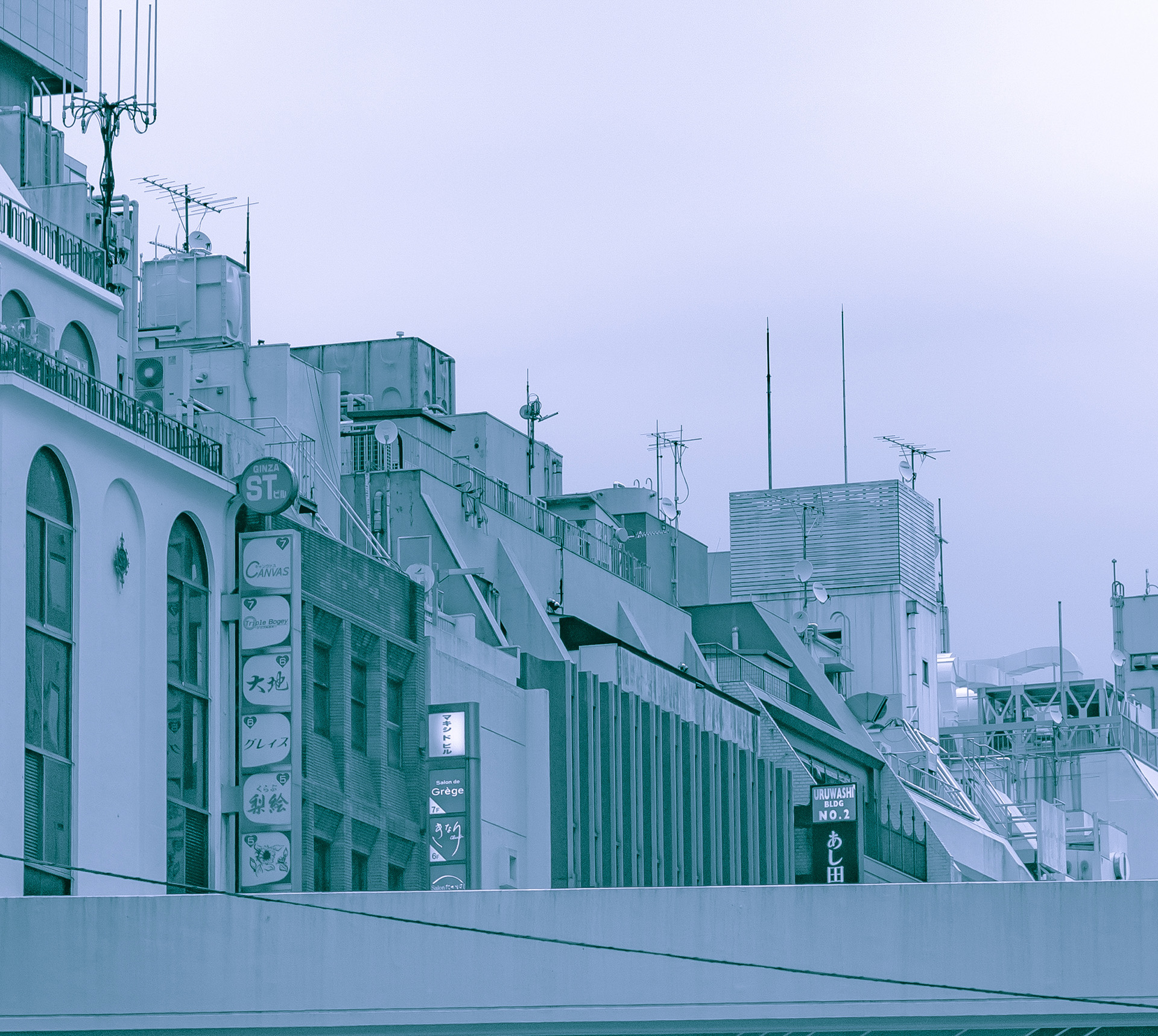 Low-contrast blue-tinted view of a set of modern concrete buildings one next to the other, their rooftops filled with satelitted dishes, antennas, and wires.